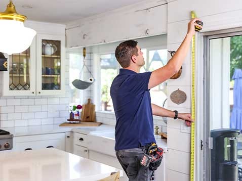 A man with a tool belt measuring a doorframe with measuring tape