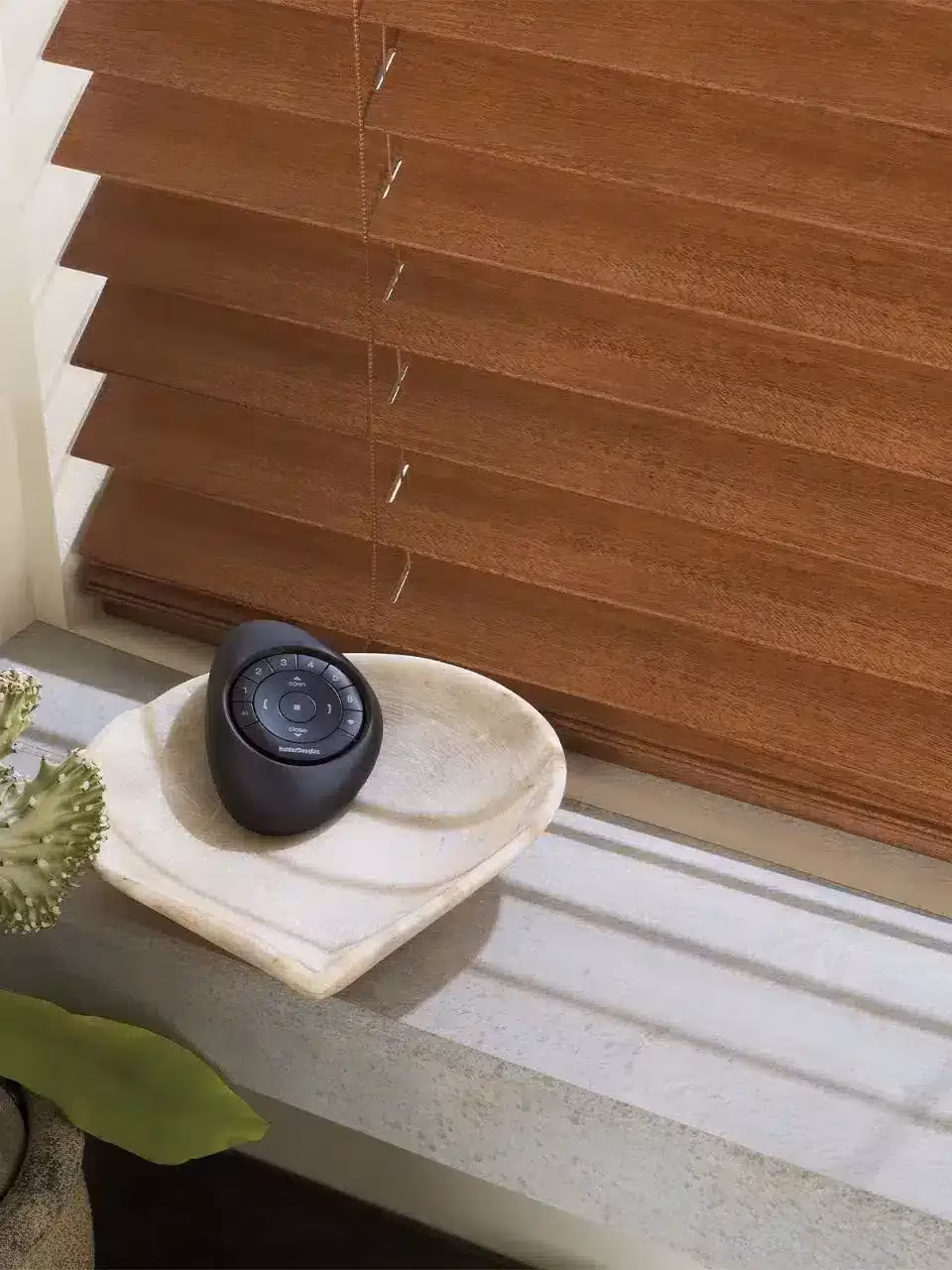 Hunter Douglas PowerView Gen 3 Pebble Remote resting in a stone dish beside mahogany Parkland wood blinds in a Healdsburg study, installed by La Grange Window Coverings